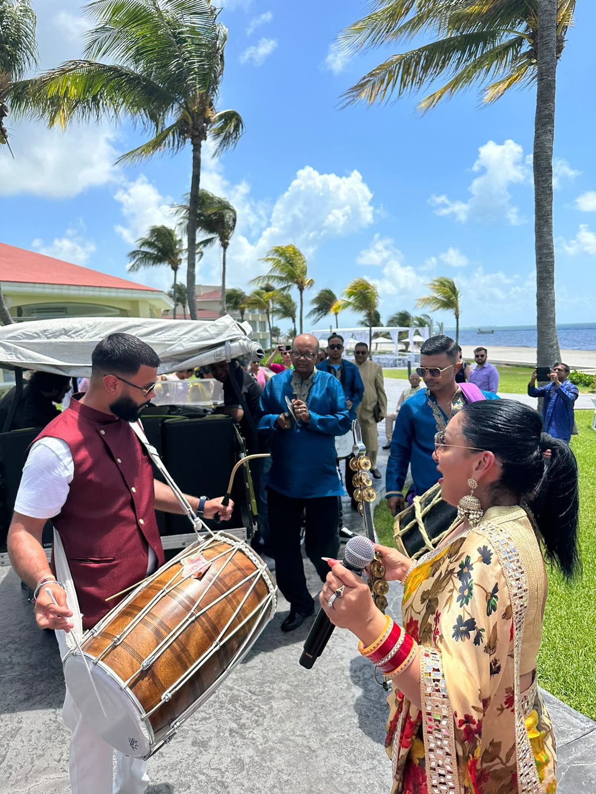 Dhol player and singer leading a baraat at a beachside destination wedding