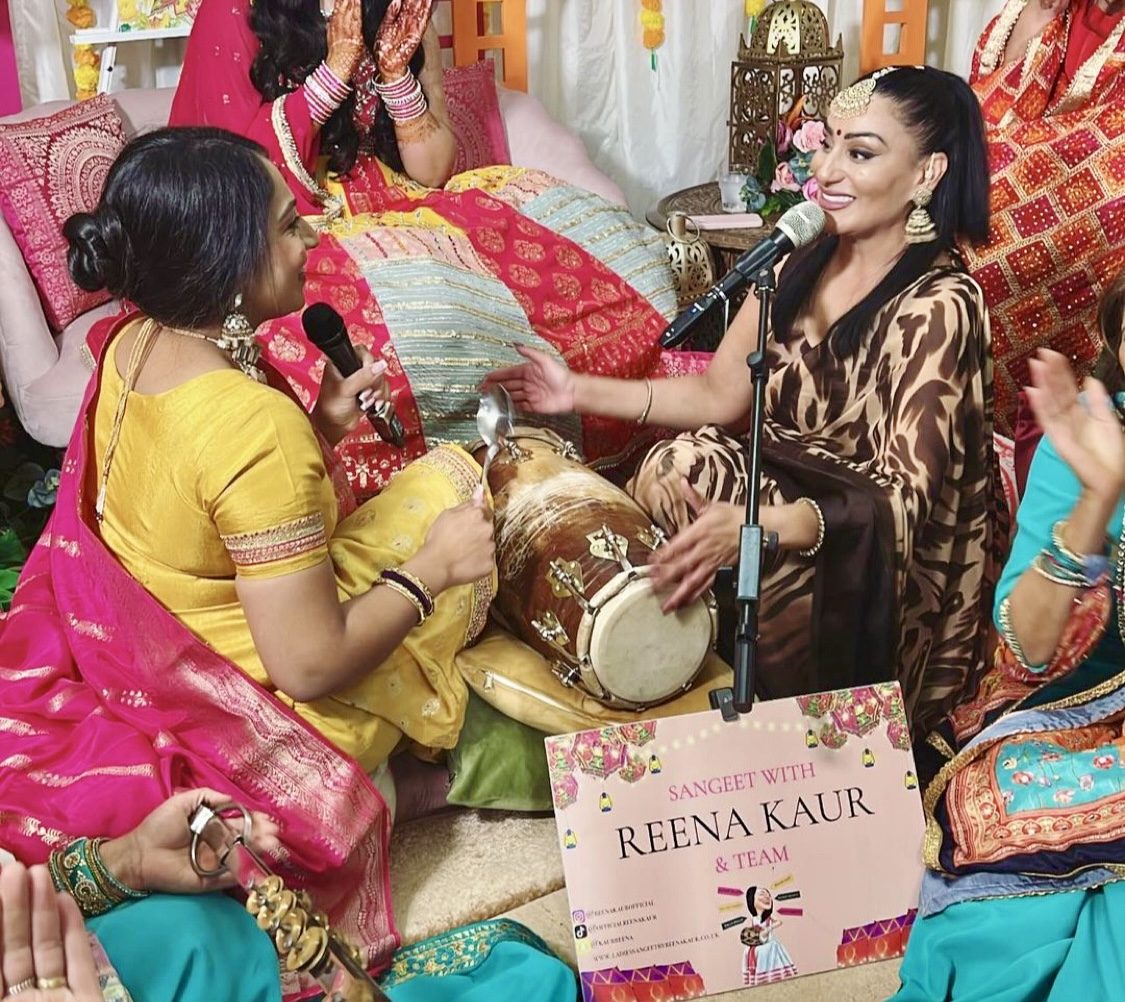 Two performers playing dholki at a Ladies Sangeet while Reena Kaur sings