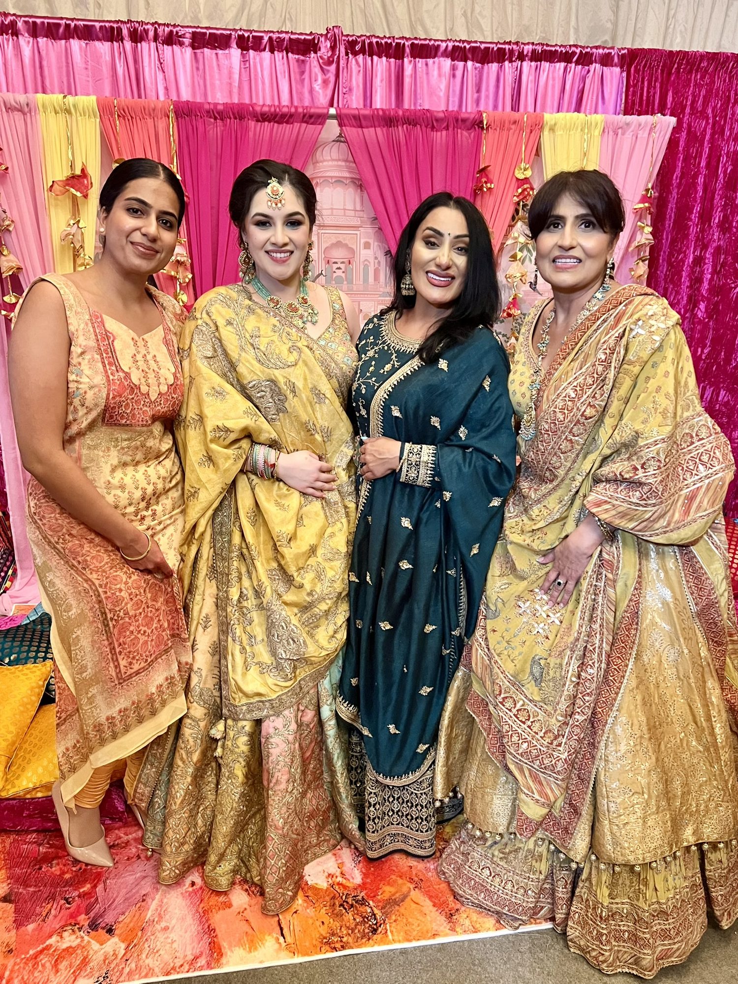 Guests at a Mehndi celebration in front of a pink and gold draped backdrop