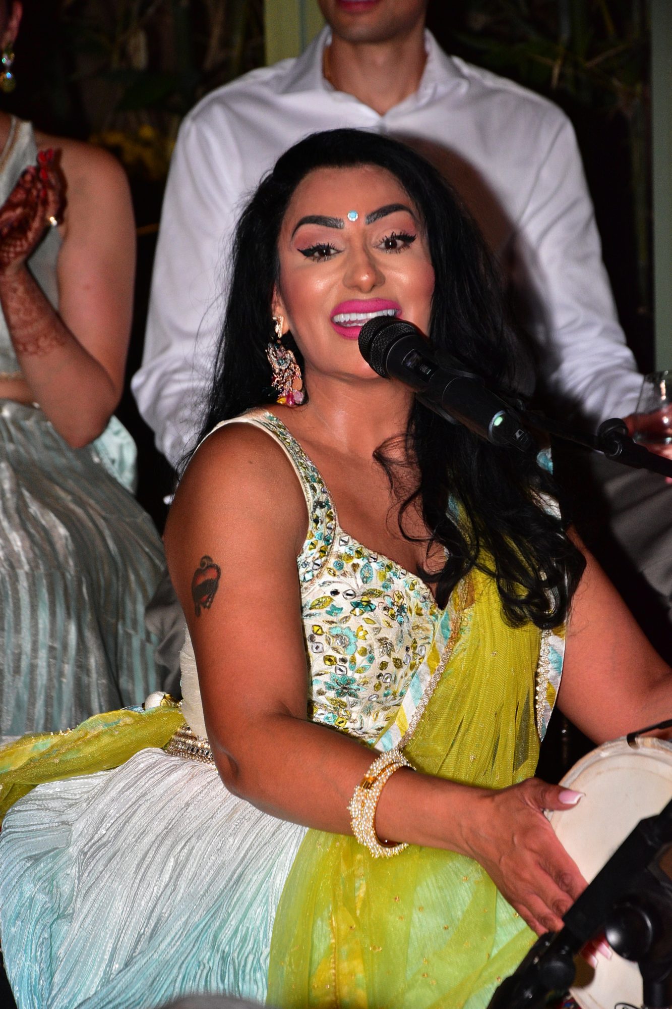 Reena Kaur singing into a microphone at a Sangeet with a dholki beside her