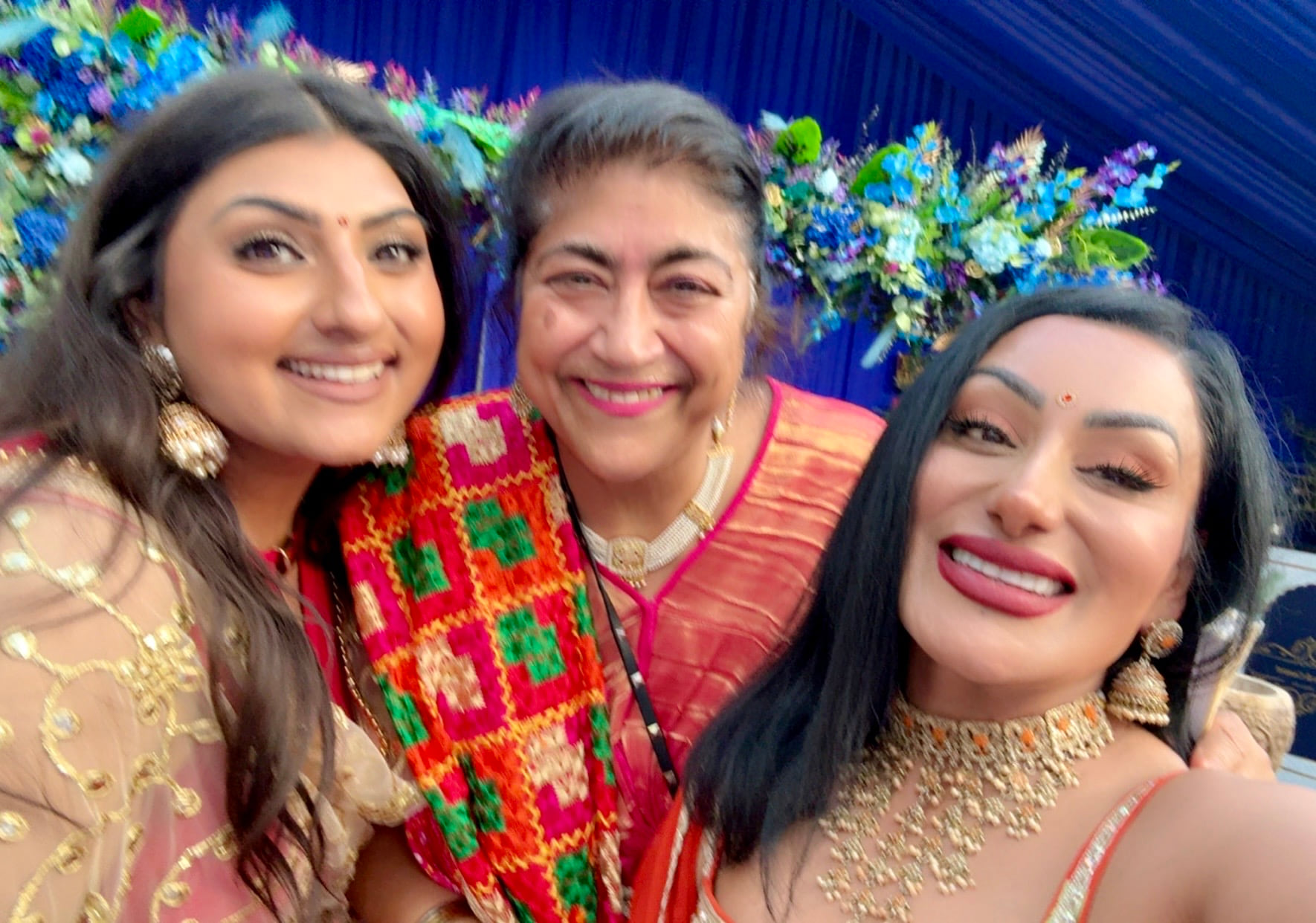 Reena Kaur with film director Gurinder Chadha and a guest in front of a floral backdrop