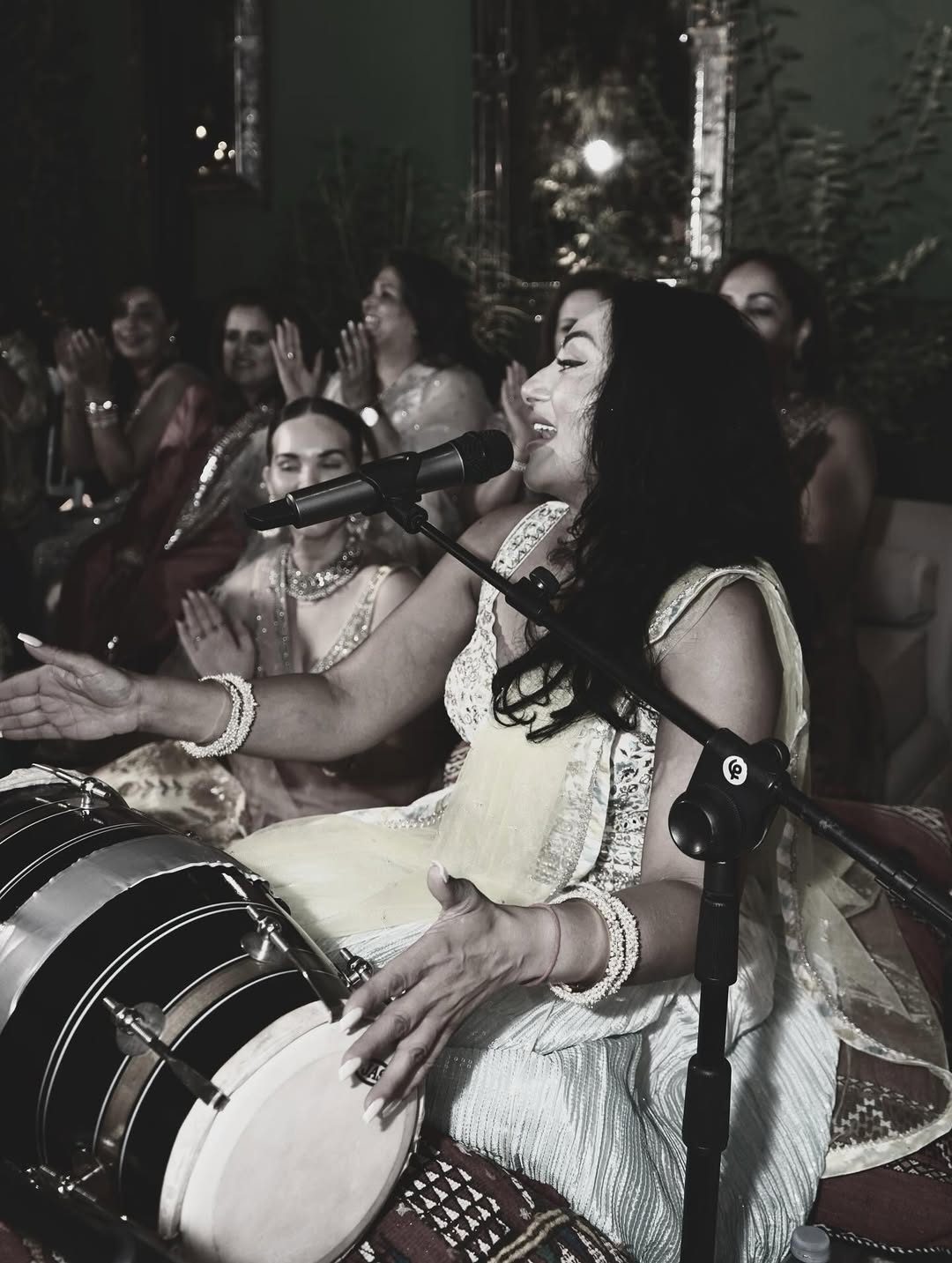 Singer performing at a Ladies Sangeet with a dholki while guests clap along
