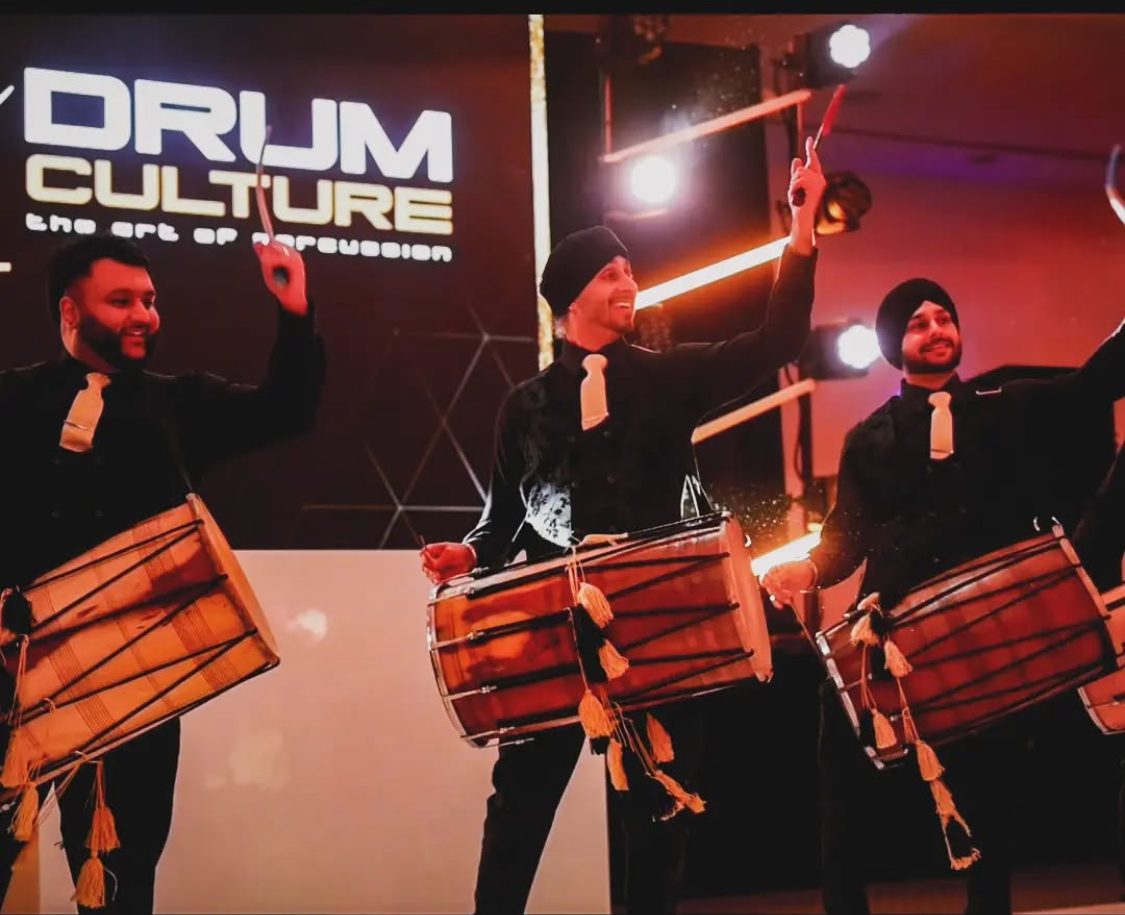 Dhol players performing together on a lit stage