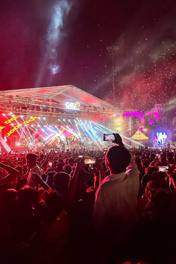 Large outdoor night-time concert stage with lighting rig, confetti and a crowd with phones raised