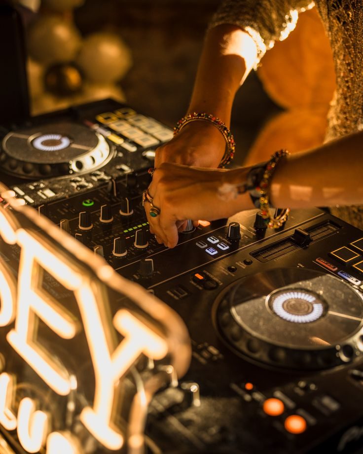 DJ mixing on professional decks beside a neon sign at an evening reception
